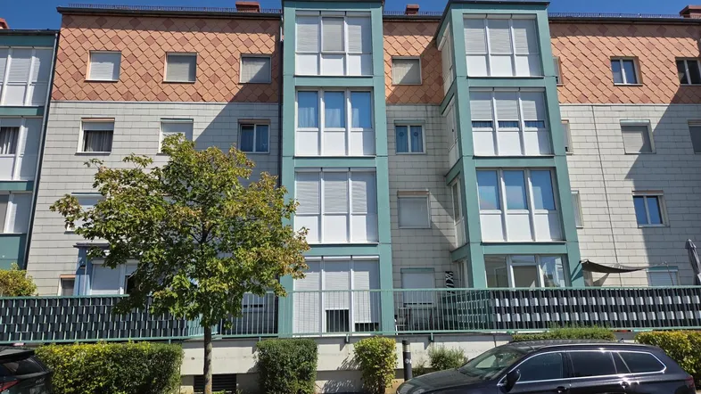 Mehrstöckiges Wohngebäude mit moderner Fassade, Balkonen und einem gepflegten Vorgartenbereich.