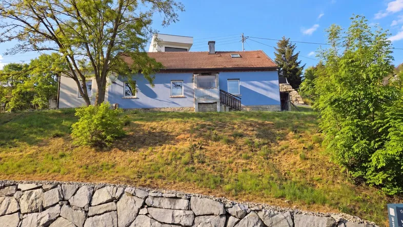 Blaues Haus auf einem Hügel mit Steinfassade im Vordergrund und grüner Umgebung.