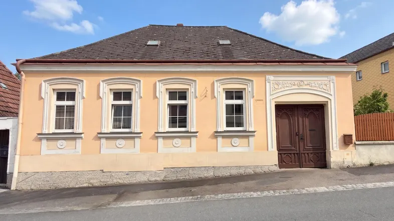Vorderansicht eines charmanten Hauses mit traditioneller Architektur und hellgelber Fassade unter blauem Himmel.