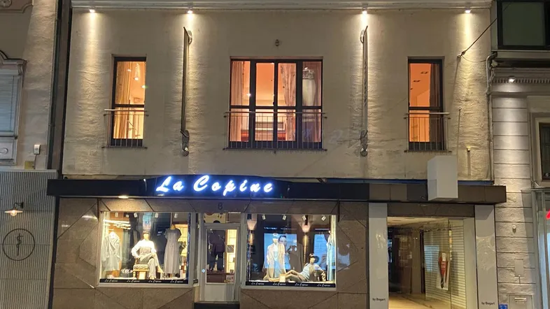 Fassade eines Gebäudes bei Nacht mit beleuchteten Fenstern und einem Ladengeschäft im Erdgeschoss.