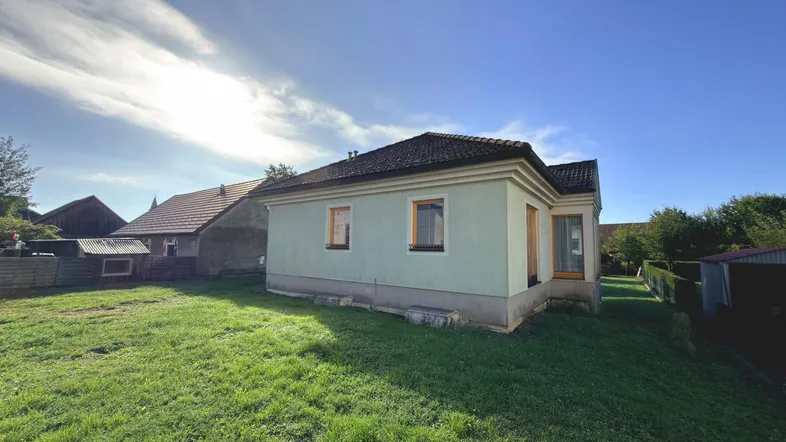 Seitenansicht des Hauses mit großem, sonnigen Rasenbereich und blauer Himmel.