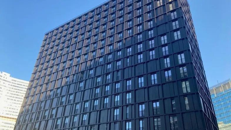 Modernes Hochhaus mit dunkler Fassade und vielen Fenstern unter klarem blauem Himmel.