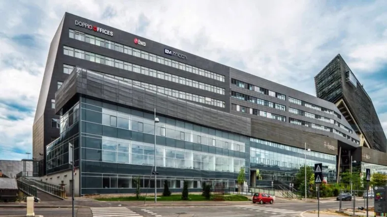 Modernes Bürogebäude mit dunkler Fassade und großen Glasflächen unter bewölktem Himmel.