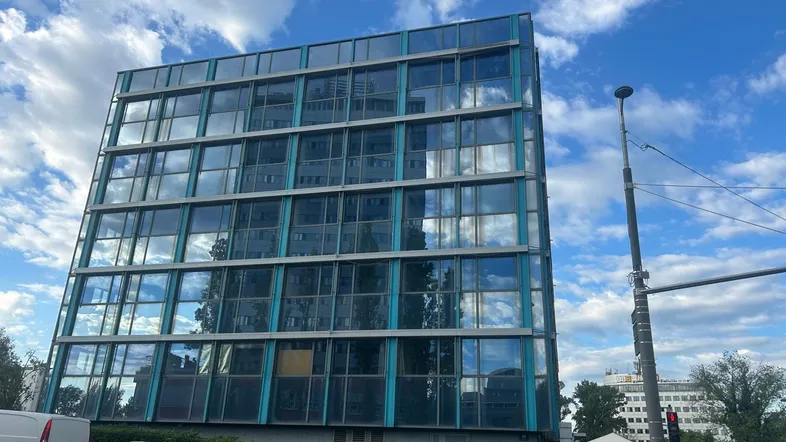 Modernes Bürogebäude mit großer Glasfassade, das den Himmel und die Umgebung widerspiegelt.
