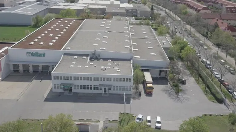 Luftaufnahme eines großen Industrie- und Bürokomplexes mit weitläufigen Parkplätzen und umliegender Bebauung.