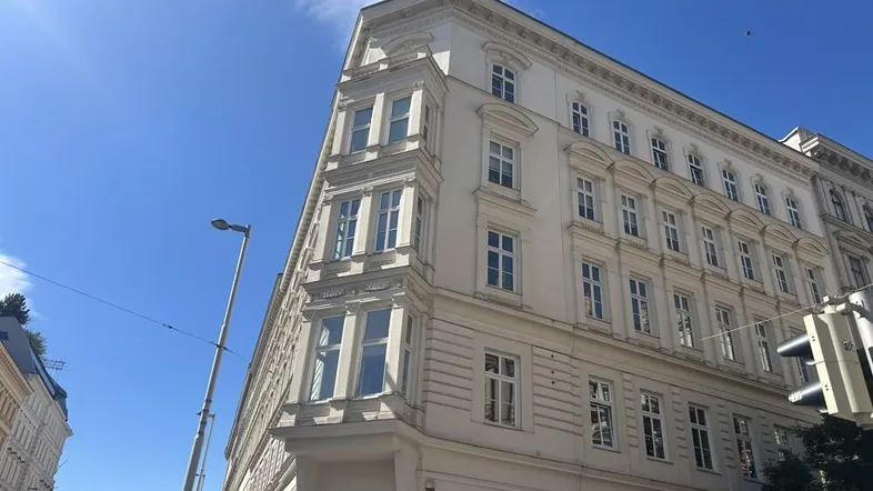 Klassisches Eckgebäude mit vielen Fenstern und historischer Architektur unter blauem Himmel.