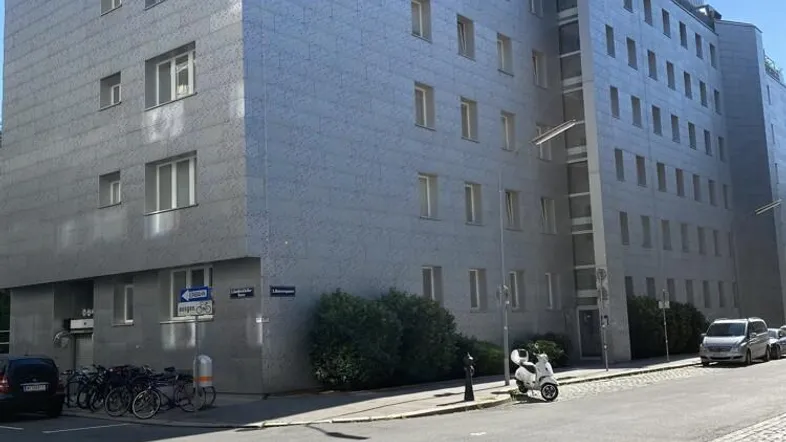 Modernes Bürogebäude mit grauer Steinfassade und vielen Fenstern an einer Stadtstraße.