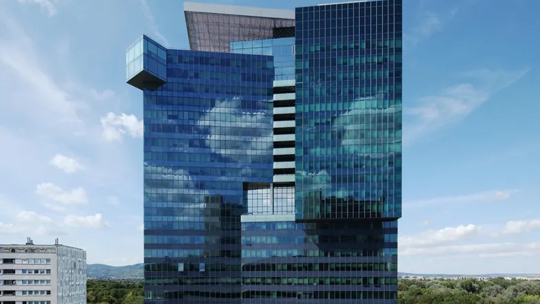 Modernes Hochhaus mit blauer Glasfassade und reflektierenden Wolken am Himmel.