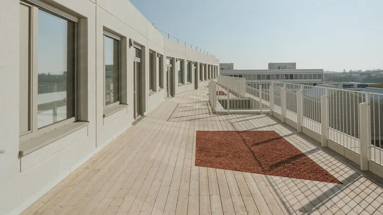 Lange Holzterrasse auf einem modernen Gebäude mit Blick auf die Umgebung unter blauem Himmel.