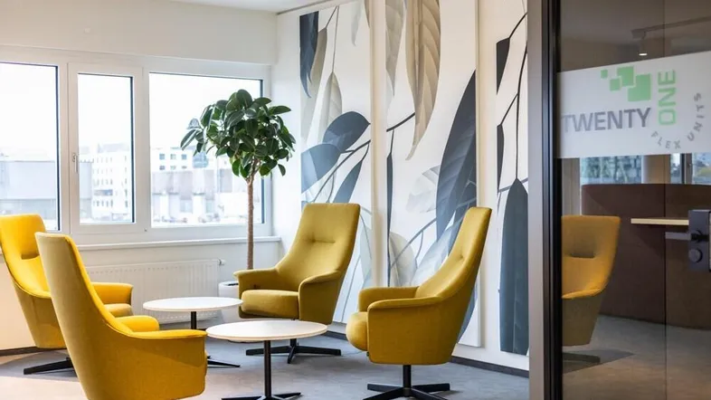 Moderner Loungebereich im Büro mit gelben Sesseln, kleinen Tischen und großen Fenstern für viel Tageslicht.