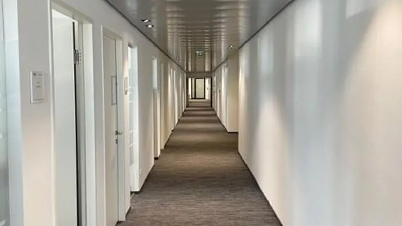 Langer, moderner Flur mit Teppichboden und zahlreichen Türen, der in die Tiefe des Gebäudes führt.