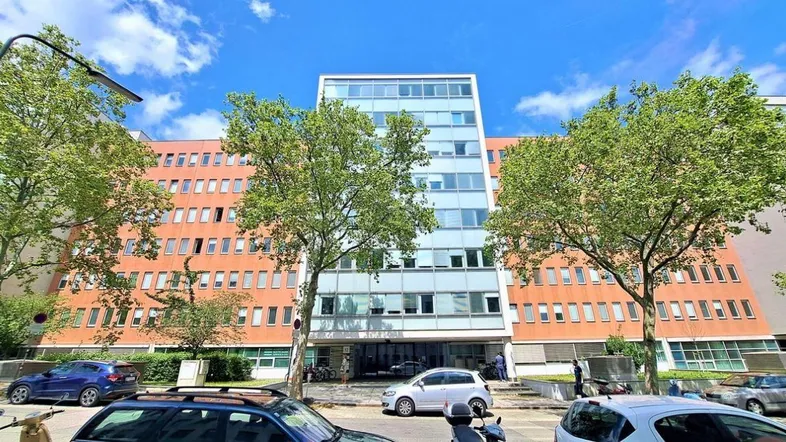 Großes Gebäude mit einer Mischung aus orangefarbener Fassade und einer modernen Glasfront im Zentrum.