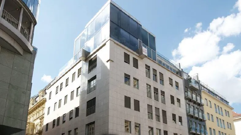 Modernes Gebäude mit heller Fassade und Glasaufbau unter blauem Himmel, in städtischer Umgebung.