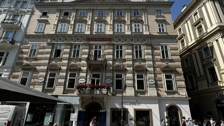 Historisches Gebäude mit aufwendiger Fassade und Geschäften im Erdgeschoss an einer belebten Straße.