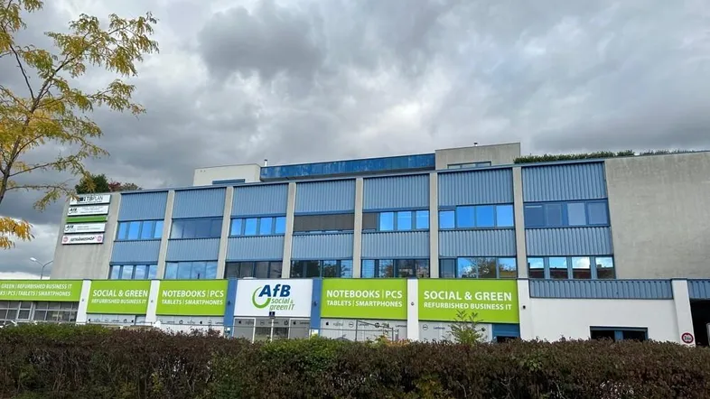 Außenansicht eines modernen Geschäftsgebäudes mit blauer Fassade und grünen Werbeschildern unter bewölktem Himmel.