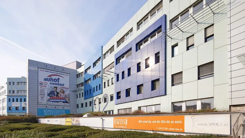 Modernes Bürogebäude mit blauen und hellgrauen Fassadenelementen unter klarem Himmel, inklusive Werbetafeln.