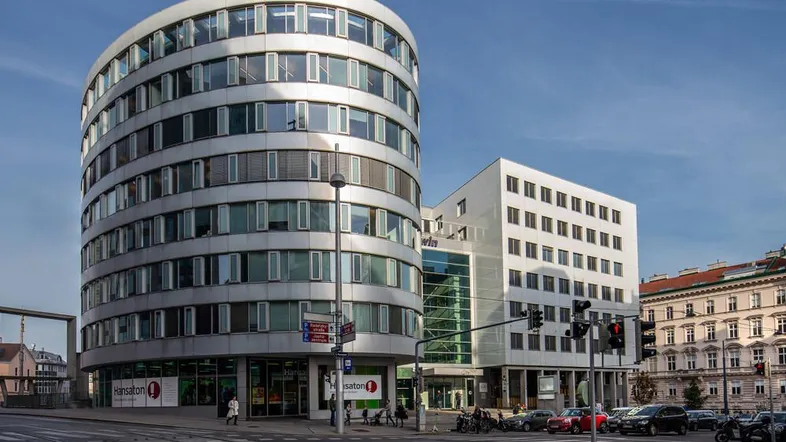 Modernes Bürogebäude mit runder Fassade und großen Fenstern an einer belebten Straßenkreuzung.
