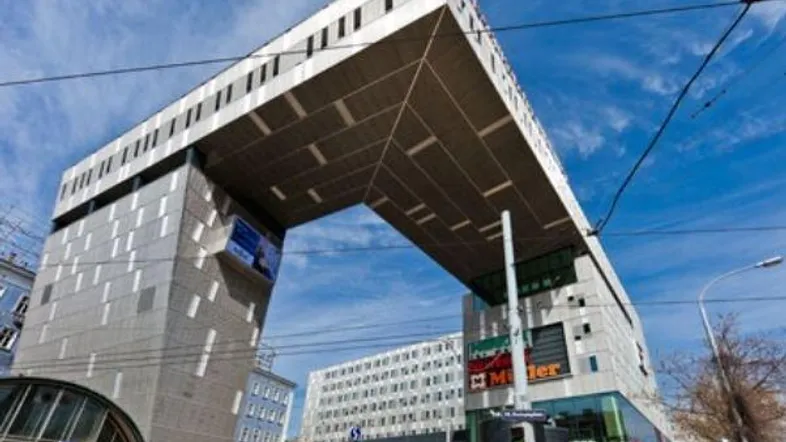 Moderne Architektur mit markantem Bogen und Glasfassaden unter blauem Himmel.