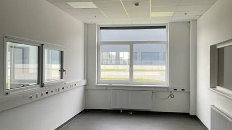 Heller Büroraum mit großen Fenstern, Fliesenboden und abgehängter Decke, ideal für Arbeitsbereiche.