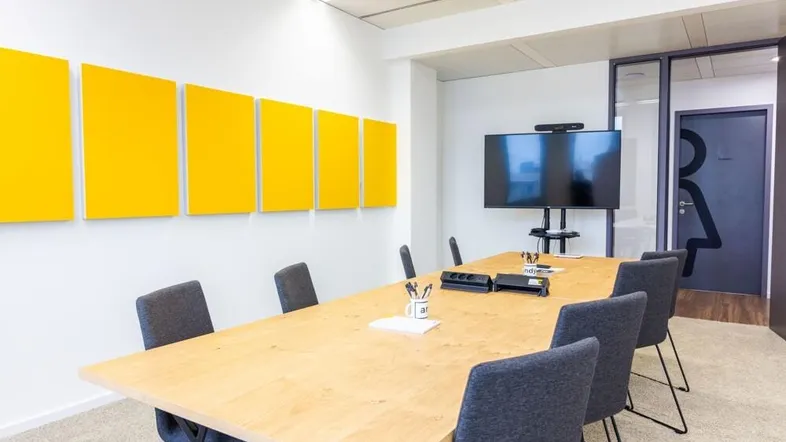 Moderner Konferenzraum mit großem Holztisch, bequemen Stühlen und einem Wandbildschirm für Präsentationen.