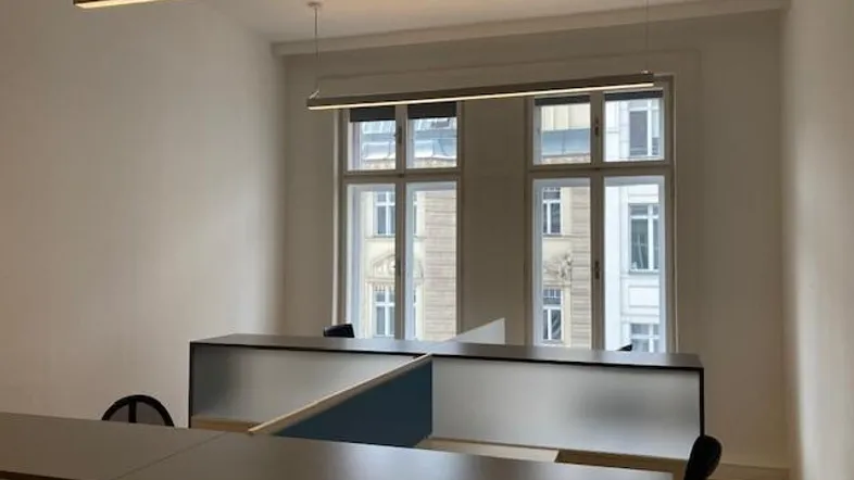 Modernes Büro mit mehreren Arbeitsplätzen, großen Fenstern und Holzparkettboden.