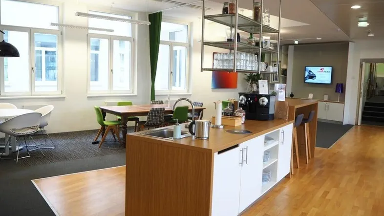 Moderne Büroküche mit Holzelementen, Kücheninsel und Essbereich, ideal für Pausen und Besprechungen.