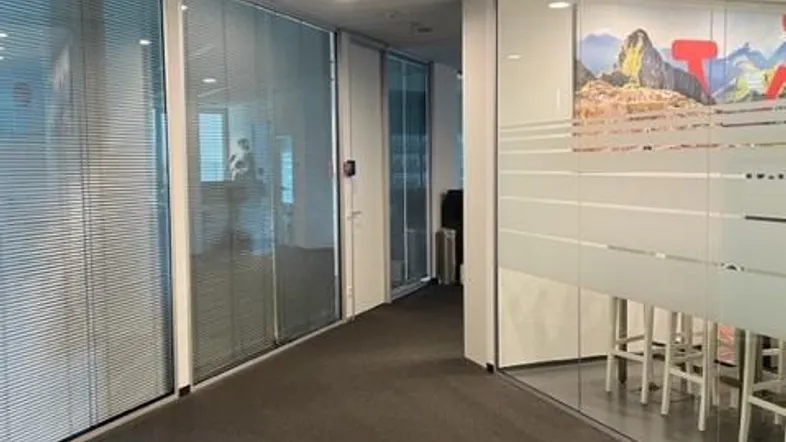 Langer Bürogang mit Teppichboden und Glaswänden, die zu Konferenzräumen führen.