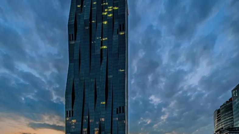 Moderner Wolkenkratzer mit dunkler Glasfassade vor einem dramatischen Sonnenuntergangshimmel.
