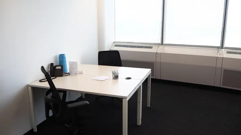 Modernes Büro mit weißem Schreibtisch, zwei Stühlen und Fenstern mit Jalousien für Privatsphäre.