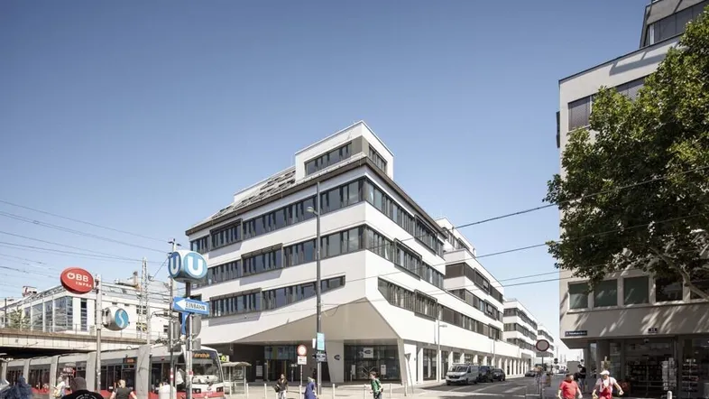 Modernes Bürogebäude an einer belebten Straßenecke mit öffentlichen Verkehrsmitteln und klarem Himmel.