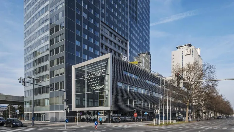 Modernes Hochhaus mit Glasfassade und angrenzendem Bürogebäude an einer belebten Straßenkreuzung.