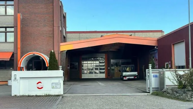 Gebäudeansicht mit Ziegelsteinfassade, großem Garagentor und überdachtem Eingangsbereich für Fahrzeuge.