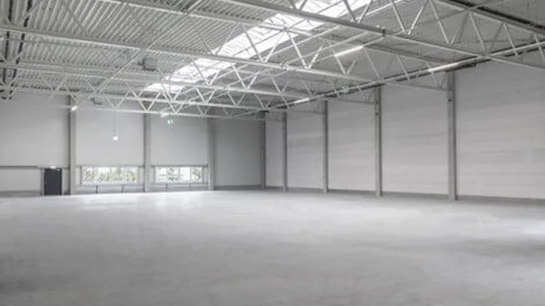 Geräumige, leere Lagerhalle mit hoher Decke, Betonboden und natürlichem Lichteinfall durch Oberlichter.