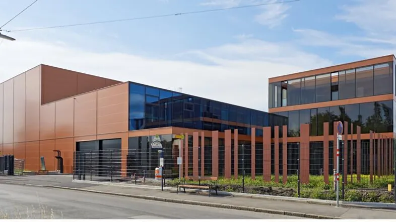 Modernes Geschäftsgebäude mit Glasfassade und braunen Paneelen an einer Straße unter blauem Himmel.