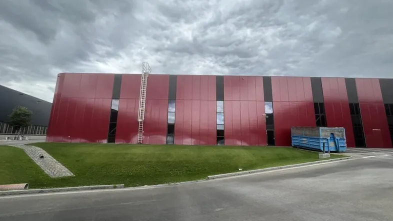 Moderne Gewerbefassade in leuchtendem Rot mit vertikalen Fenstern und Grünfläche.