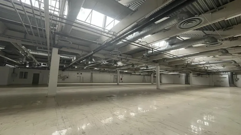 Großer, leerer Industrieraum mit hohen Decken, sichtbaren Lüftungskanälen und viel Tageslicht durch Oberlichter.