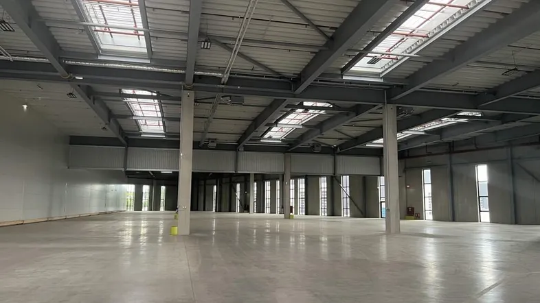 Große, leere Lagerhalle mit hohen Decken, Betonboden und Oberlichtern für viel Tageslicht.