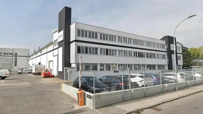 Modernes Geschäftsgebäude mit weißer Fassade, schwarzen Akzenten und großem Parkplatzbereich davor.