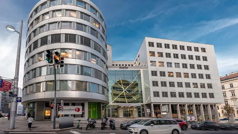 Modernes Bürogebäude mit markanter runder Fassade und großen Fenstern an einer belebten Stadtkreuzung.