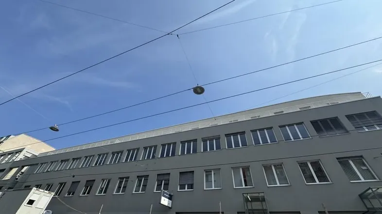 Graues Geschäftsgebäude mit vielen Fenstern unter blauem Himmel, im Vordergrund sind Baucontainer sichtbar.