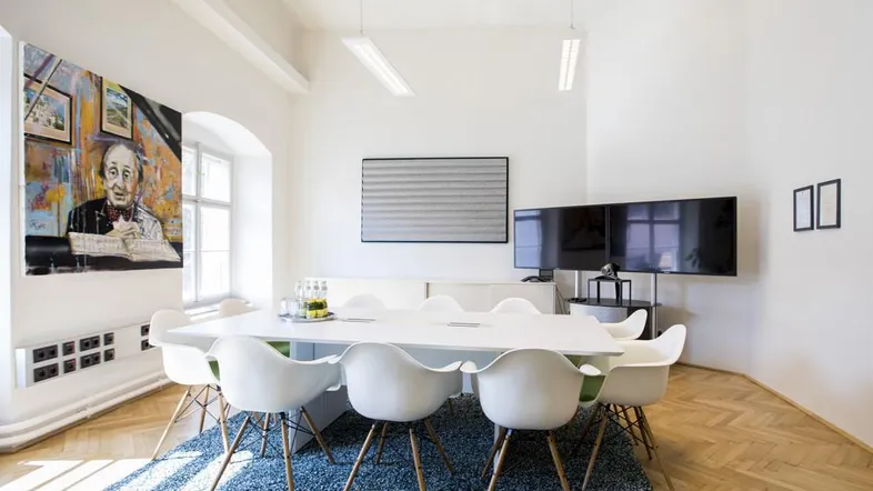 Heller Konferenzraum mit modernem Design, großem Tisch, bequemen Stühlen und Kunstwerken an den Wänden.