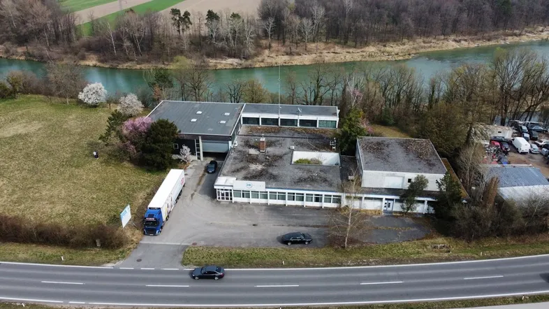 Luftaufnahme eines Gewerbeobjekts mit mehreren Gebäuden, angrenzender Straße und Fluss im Hintergrund.