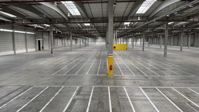 Geräumige, leere Lagerhalle mit hohen Decken, Betonboden und natürlichem Lichteinfall durch Oberlichter.