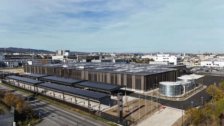 Luftaufnahme eines großen Industriegebäudes mit Solaranlage auf dem Dach und überdachten Parkplätzen.
