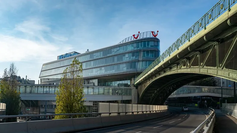 Modernes Gebäude mit geschwungener Glasfassade neben einer Brücke und einer Straße unter blauem Himmel.