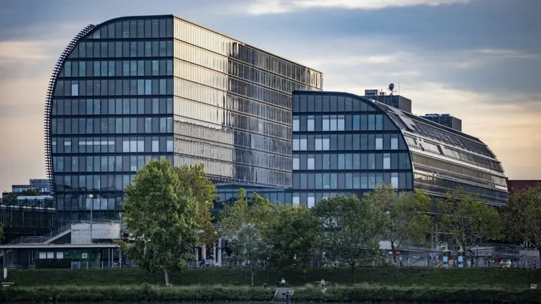 Modernes Bürogebäude mit geschwungener Glasfassade am Flussufer bei Sonnenuntergang.