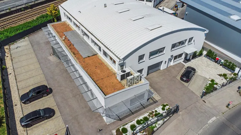 Luftaufnahme eines modernen Bürogebäudes mit geschwungenem Dach, Gründach und Parkplätzen.