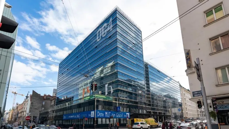Modernes Bürogebäude mit Glasfassade an einer belebten Stadtstraße und klarem Himmel.