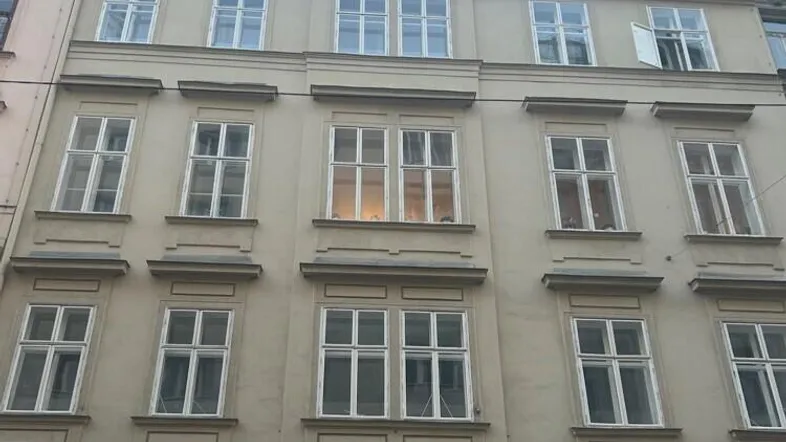 Klassisches Mehrfamilienhaus mit vielen Fenstern und Geschäften im Erdgeschoss in einer Stadtansicht.