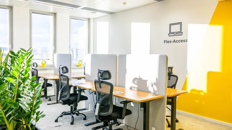 Moderner Büroraum mit mehreren Arbeitsplätzen, großen Fenstern und einer gelben Akzentwand.